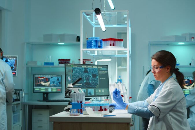 Medical lab worker analyzing blood serum conducting virus test in modern equipped lab late at night. Team of specialists examining vaccine evolution using high tech for treatment against covid19